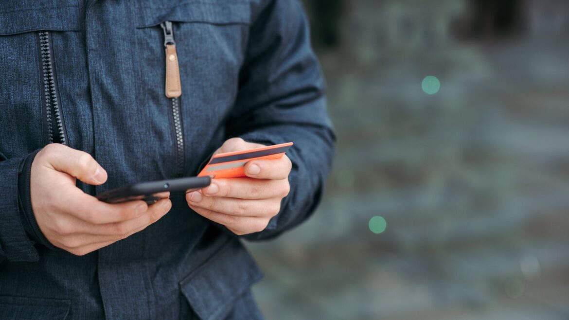 Homme en tenue casual saisissant les détails de sa carte bancaire sur smartphone, en extérieur