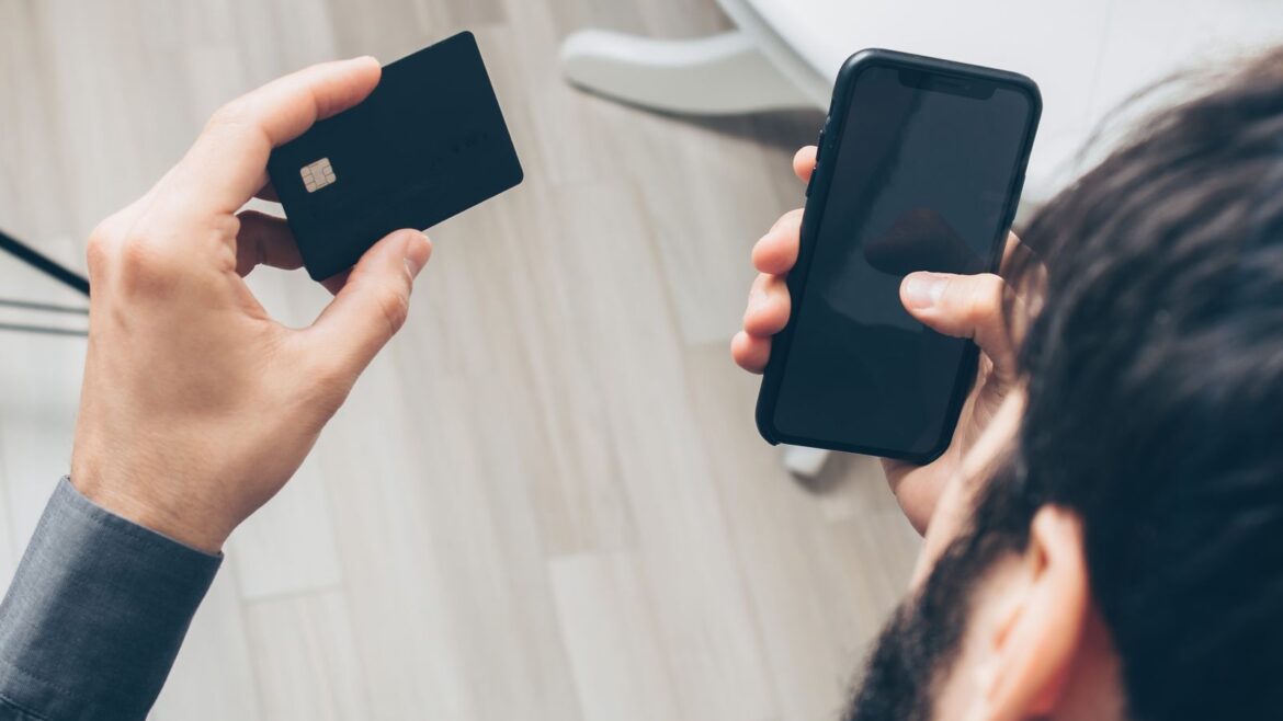 Homme tenant un smartphone et une carte bancaire pour un paiement en ligne