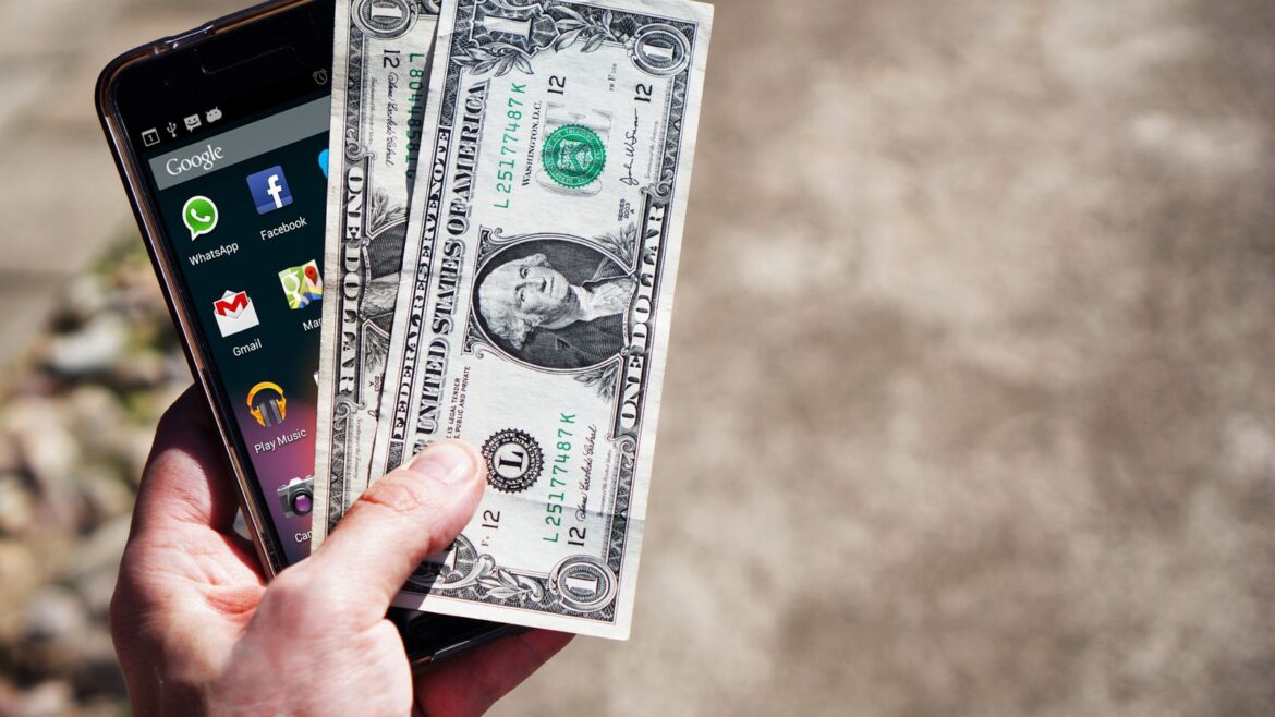 Main tenant des billets de dollars et un smartphone en extérieur pour parier