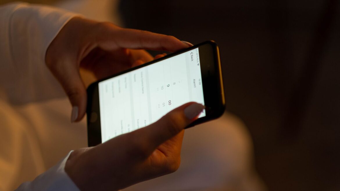 Mains réglant une alarme sur un smartphone de nuit pour parier