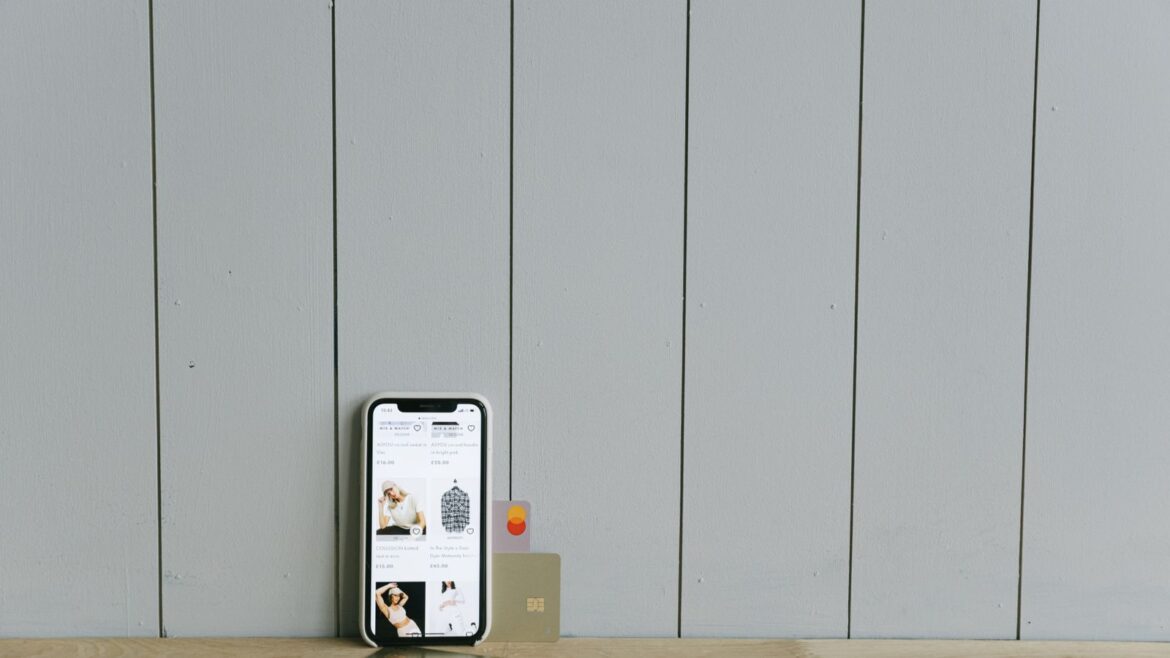Smartphone affichant un site marchand avec carte bancaire posée sur une table en bois